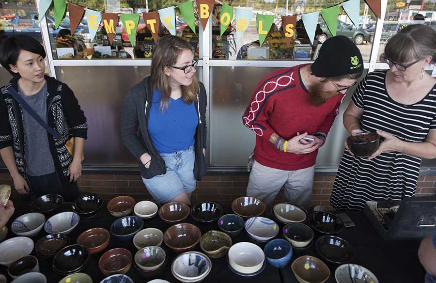 Nik Price, a graduate student in printmaking from Mankato, Minn., inspects the design on a ceramic bowl held by SIU associate professor of ceramics Pattie Chalmers, alongside graduate students in ceramics Yen-Ting Chiu, of Taipei, Taiwon, and Kari Woolsey, of Boca Raton, Fla., on Saturday, Oct. 15, 2016, during the Empty Bowls fundraiser outside The Neighborhood Co-op Grocery in Carbondale. Chalmers said the best part of the event will be giving a big check to the Good Samaritan House. "It's also been great meeting the community and for the students, the makers of the bowls, to be out here selling their creations," Chalmers said. (Morgan Timms | @Morgan_Timms)