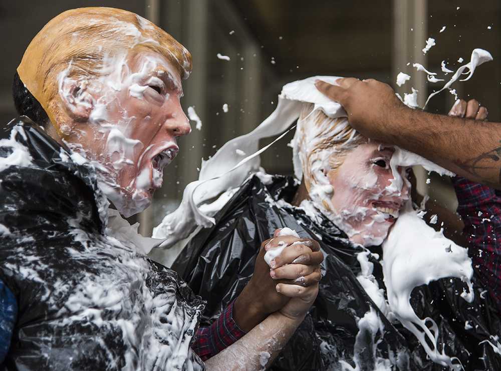 Dakota Oria, a junior from Chicago studying computer science, left, and Donquell Sanders, a sophomore from Chicago studying biological science, brace themselves as Christopher Regalado, a junior from Chicago studying architecture, hits them with a plate of shaving cream Tuesday, Nov. 8, 2016, in the Faner Breezeway. Members of Dedicated Young Latinos Embodying Success asked passersby for $1 donations to "pie" either candidate as a fundraiser for Toys for Tots. "At the moment we're just trying to lighten the mood of the election," Oria said of the fundraiser. "Even though both sides are bad, it doesn't mean we can't have a little bit of fun." (Morgan Timms | @morgan_timms)