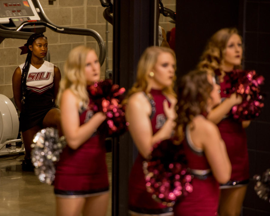 Sophomore cheerleader, Alaysia Brandy, kneels behind Saluki Shakers during the national anthem Monday, Nov. 27, 2017, during the Salukis loss to the SIU Edwardville Cougars at SIU Arena. A recent change in protocol put into place by SIU Athletics has removed the cheerleaders from the playing surface of sporting events during the national anthem. (Brian Munoz | @BrianMMunoz)