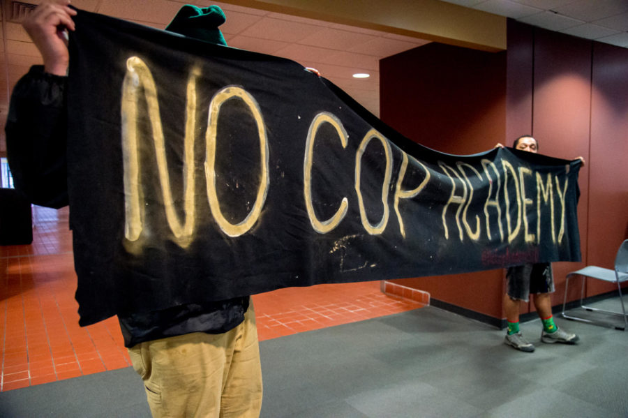 Demonstrators hold up a banner Thursday, March 29, 2018, during a demonstration against a proposed police academy at Southern Illinois University in the student center. (Brian Munoz | @BrianMMunoz)