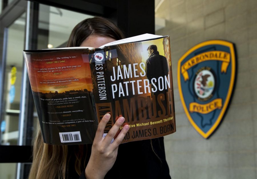 Staff writer, Rana Schenke, reads Ambush by James Patterson in the lobby of the Carbondale Police Station, Wednesday, Oct. 17, 2018. (Allie Tiller | @allietiller_de)