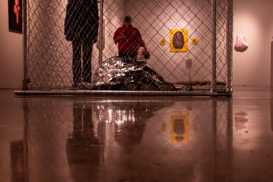 A woman sits silently under an emergency blanket inside a cage as part of a live art piece at SIUs Love at the Glove art show. Other performers walked around in underwear covered in bruises and scratches silently bringing up the topic of abuse and sex trafficking.