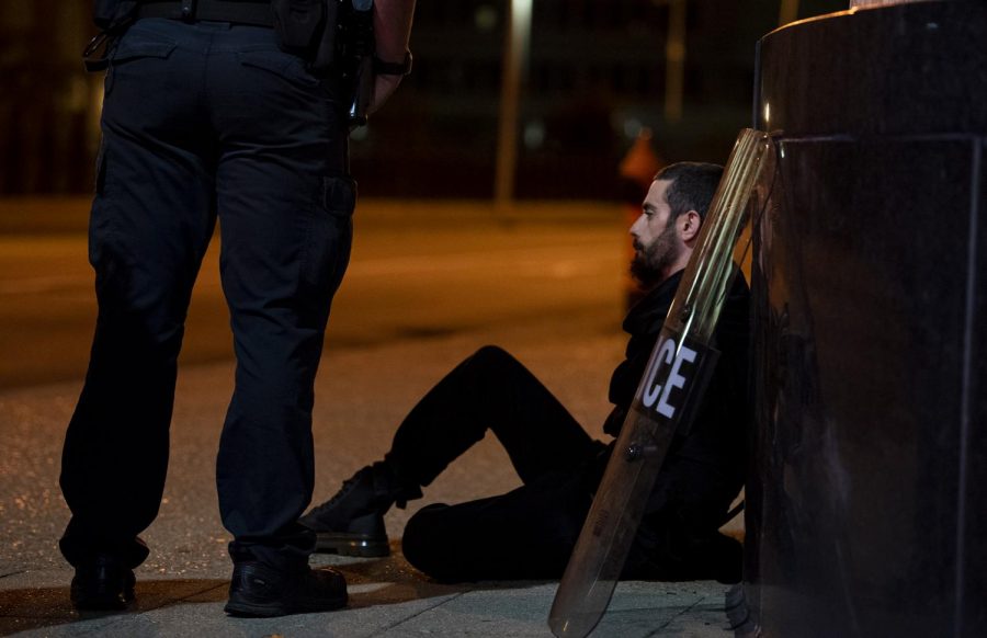 A man sits on the sidewalk as waits to be taken into police into police custody on West Broadway and South 6th St. after being out past the 9pm curfew, which was put in place in the wake of the Breonna Taylor grand jury decision, in Louisville, Ky.  