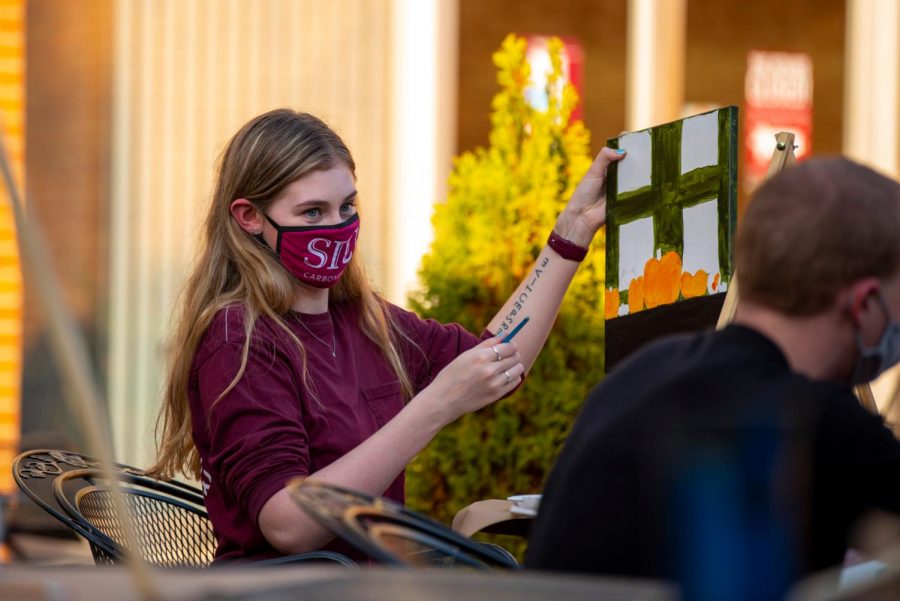SIU student, Jordan Smearman, shows off the progress on her painting during the Painting on the Patio event at the outside of the Student Center Wednesday, Oct. 21, 2020. The event held a limited amount of people where painters could gather together to paint a fall themed subject.