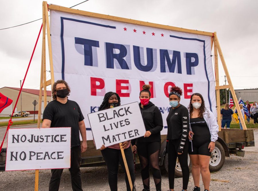A group of Black Lives Matter protesters pose for a photo in front of a Trump banner at the Trump Train event in Anna, Ill., on Saturday, Oct. 10, 2020. This was the second Black Live Matters protest held in Anna, Ill. this year. 