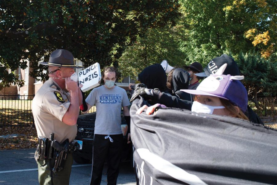 A local law enforcement officer tries to calm the crowd as they block off the road for passing Trump supporters Saturday, Oct. 17, 2020, in  Carbondale, Ill.