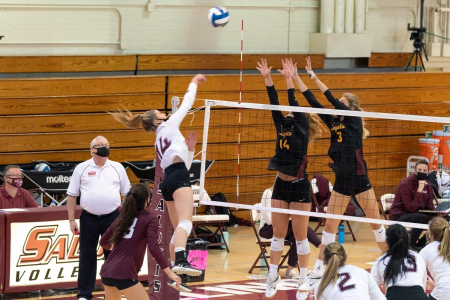 Taylor Morgan (14), with a huge leap, spikes the ball towards the opponents side of the court in front of two blocking opponents from Loyola University on Sunday, Feb. 7, 2021, in Davies Gym at SIU.