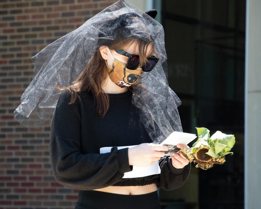 Hannah Combs, a student in the Department of Cinema, reads messages about the extinction of animals due to climate change during the funeral casket procession  in honor of countless species of animals that have gone extinct on Thursday, April 22, 2021 at the Communications Building in Carbondale, Ill. 