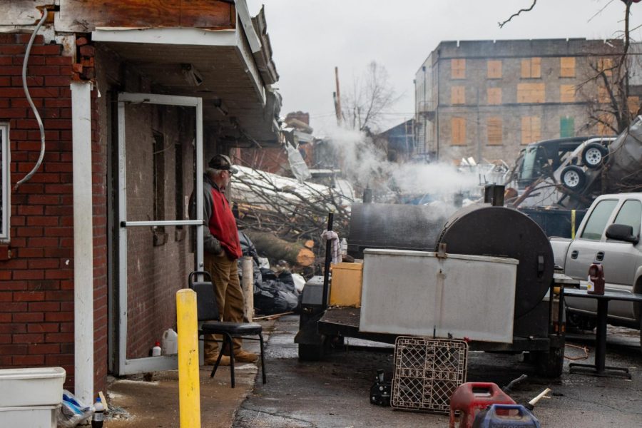 A volunteer stands outside of what used to be Fowlers K&N Root Beer to cook and serve sandwiches to the community and volunteers Dec. 17, 2021 in Mayfield, Kentucky. 