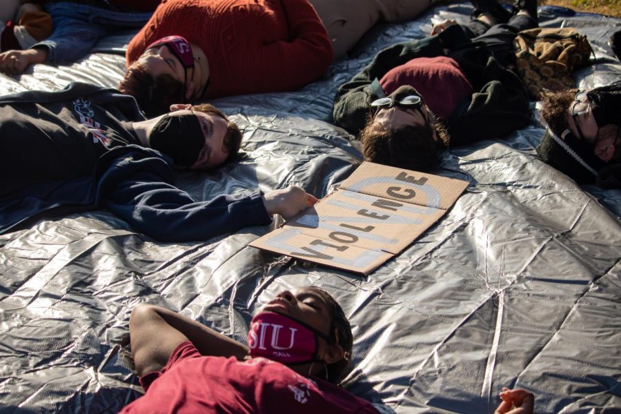 Jason Isele holds a poster that says, End Violence, as they lie in front of Anthony Hall during the die-in protest Dec. 1, 2021 at SIU in Carbondale, Illinois. 