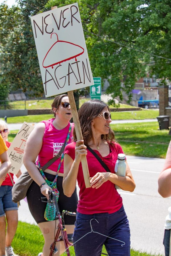 A woman olds a sign that says, Never Again, with a hanger in her belt loop at the Bans Off Our Bodies March May 14, 2022 in Carbondale, Ill. 