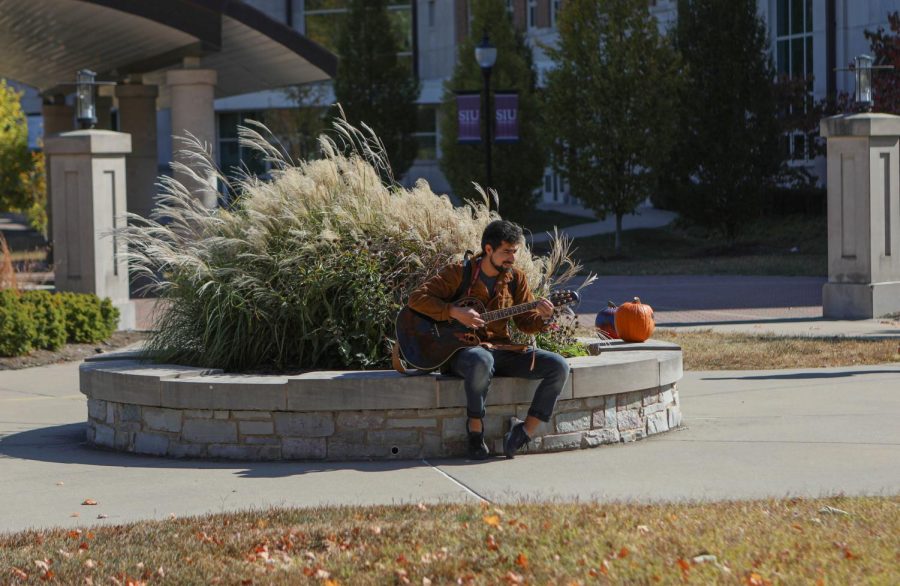 An SIU Student sits on a ledge and strums his guitar Oct. 21, 2022 at Faner Plaza in Carbondale, Ill.