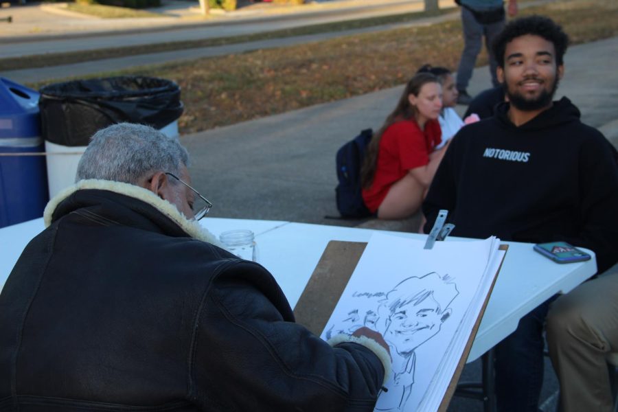 Students sit in front of the caricature artist Oct. 13, 2022 at the campus block party in Carbondale, Ill. 
