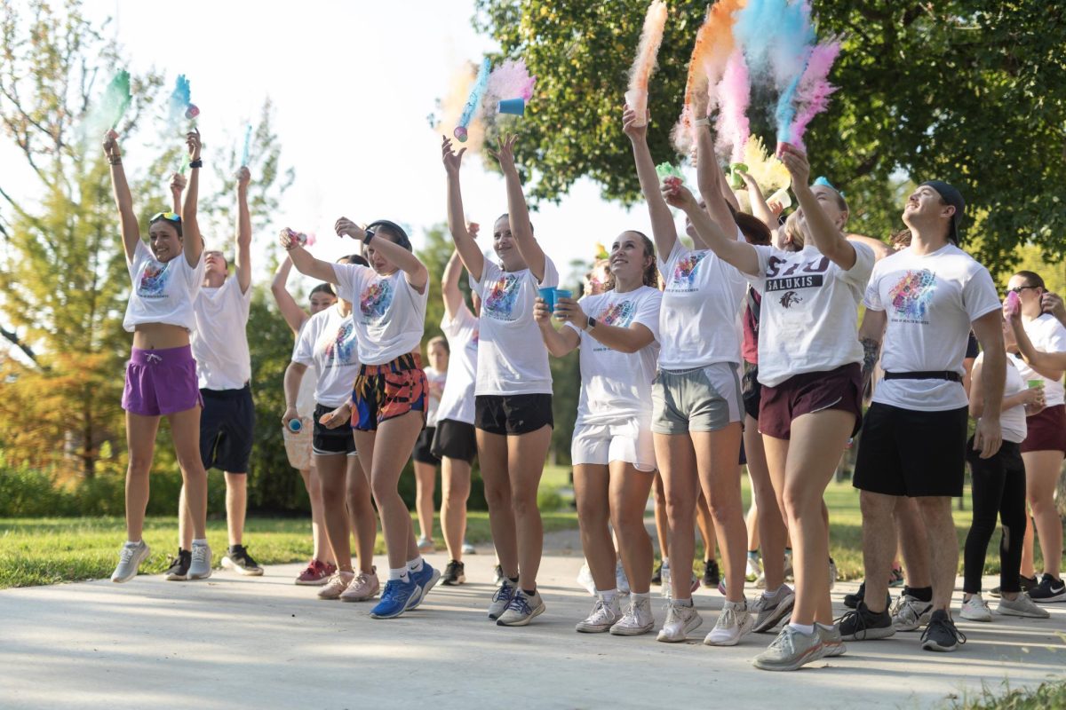 Racers of the third annual Color Fun Run, hosted by the School of Health Sciences, toss cups of colored powder up in the air as the race begins Sept. 29, 2023 at the Campus Lake in Carbondale, Illinois. 