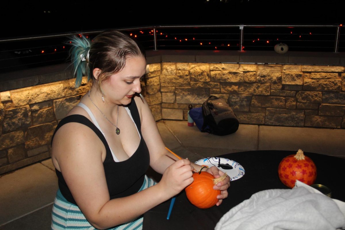 SIU sophomore Zipporah Puffer paints a pumpkin during Moonlight on the lake Oct. 24, 2023 at Becker Pavilion in Carbondale, Illinois.