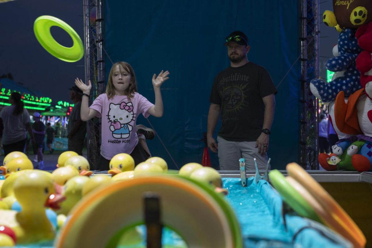 Jemma Farmer, of Mt. Vernon, Illinois, tosses a ring towards rubber ducks in an attempt
to win a prize from the booth while her father, Jim Farmer, watches Aug. 23, 2024 at the
Du Quoin State Fair in Du Quoin, Illinois. @lyleegibbsphoto