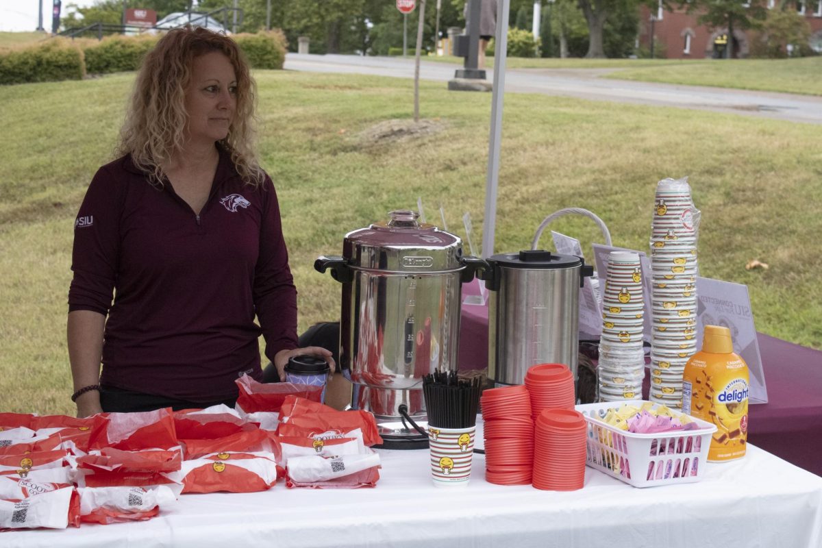 Tibretta Reiman stands under the
canopy to get away from the rain as
they wait for students to come for
their giveaway of coffee and donuts.