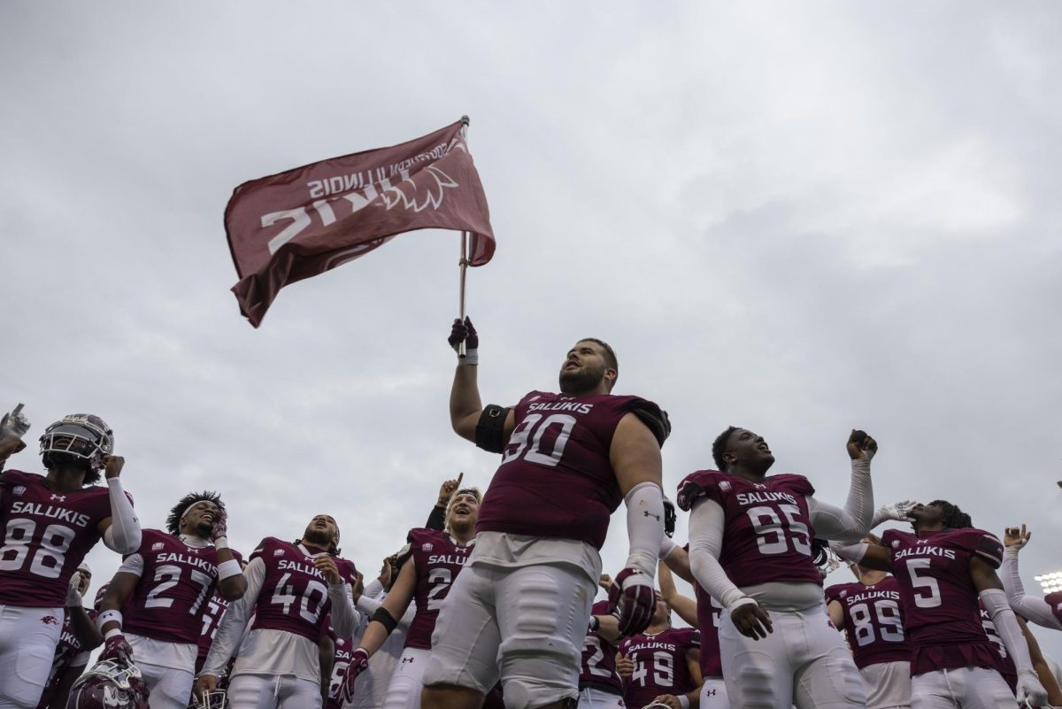 Peyton Reeves (90) holds an SIU flag and sings the school fight song alongside his teammates who stand behind him after the Salukis picked up a win over Youngstown State at home, ending a six-game losing streak Nov. 9, 2024 at Saluki Stadium in Carbondale, Illinois. 