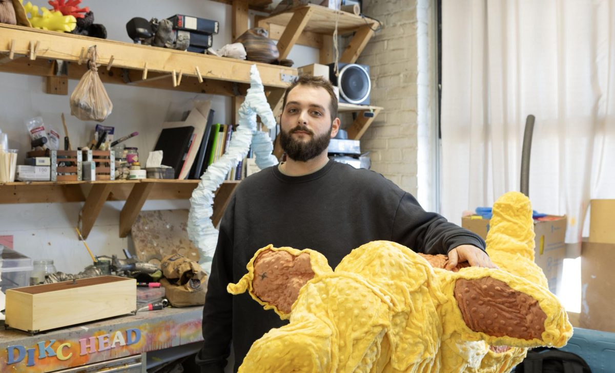 Second year graduate student Brenden Deasy, rests his arms across his art piece “Turn on your listening ears and press mine,” Feb. 6, 2026 in one of his studios at the Glove Factory in Carbondale, Illinois. Deasy is pursuing a Master of Fine Arts in Sculpture. This is his second year submitting art to Love at the Glove. 