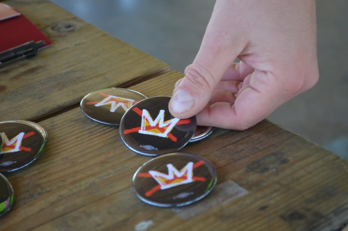 A protester picks up a No Kings logo button to wear during the 'No Kings' protest March 28, 2026 at Turley Park in Carbondale, Illinois.
