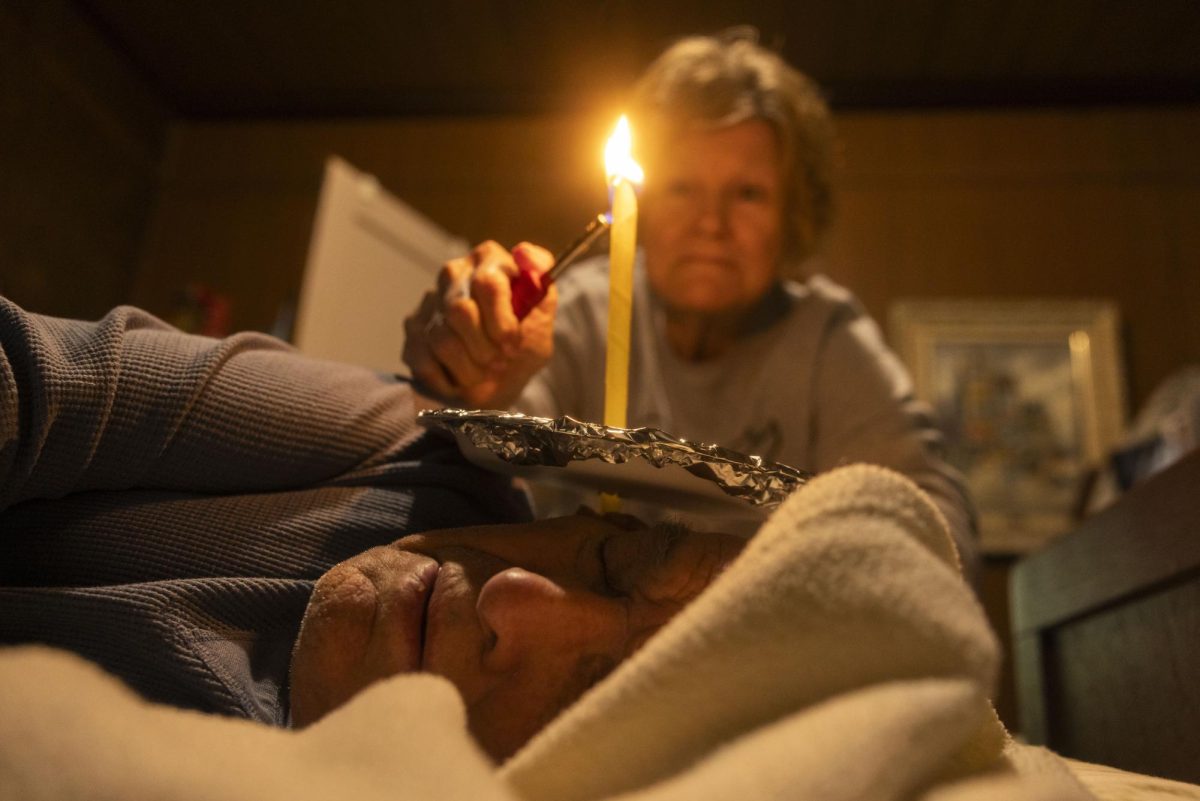 Leslie Ellis, a caretaker for 99-year-old for Kenny Moore, lights a hollow candle to withdraw earwax from Moore's ear as he lays in his bed April 11, 2026 in Murphysboro, Illinois.
